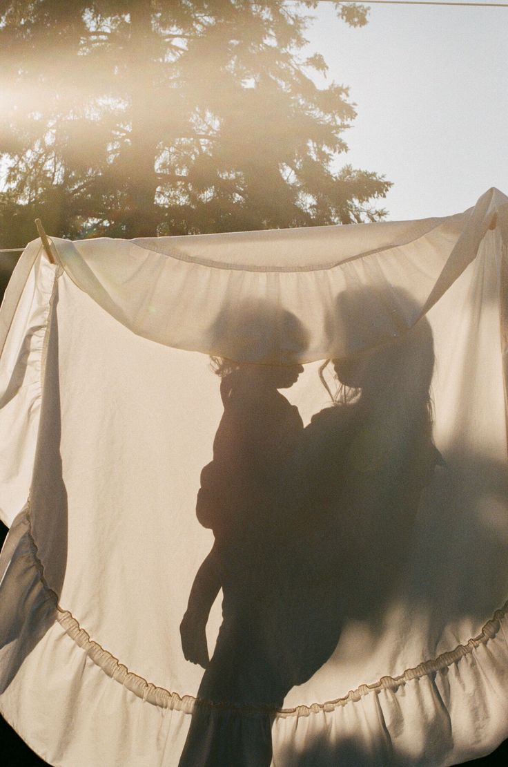 two people standing in front of a white sheet with trees in the background and sun shining on them