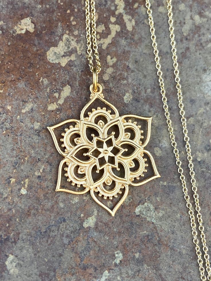 "24K Gold Plated Lotus Flower Mandala Pendant Necklace In this busy world where time is precious, the graceful petals of the lotus remind you to continue seeking out enlightenment and time for yourself to just be. Consider this 24K satin gold plated openwork lotus mandala a symbol of wholeness, meditation, and healing. In this many petaled flower charm, the lotus becomes a mandala - a visually appealing, overlapping, geometric form that helps quiet chattering thoughts, appeasing the spirit. From its center to its rim, this mandala's symmetry and beauty is exquisite. Drop onto a finished chain, and this necklace becomes a great gift for friends going through difficult transitions, like a far away move, loss of a loved one, or a career change. All the open spaces between the petals afford yo Gold Flower Jewelry With Intricate Design, Gold Flower Jewelry For Meditation, Gold Floral Jewelry For Festivals, Spiritual Gold Flower Necklaces, Gold Spiritual Flower Necklaces, Gold Spiritual Flower Necklace, Spiritual Gold Flower Pendant Necklace, Spiritual Gold Flower Necklace With Flower Charm, Spiritual Gold Necklace With Flower Pendant