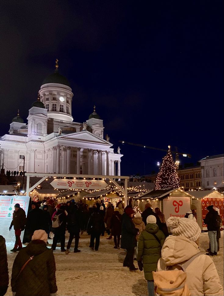 many people are walking around in front of a building with christmas lights and decorations on it