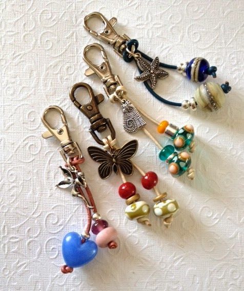 several key chains with charms attached to them on a white tablecloth background, one has a blue heart and the other is a red bow