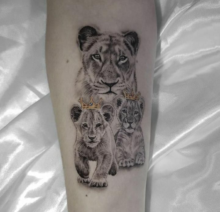 a lion tattoo with three cubs on the leg and one is wearing a gold crown