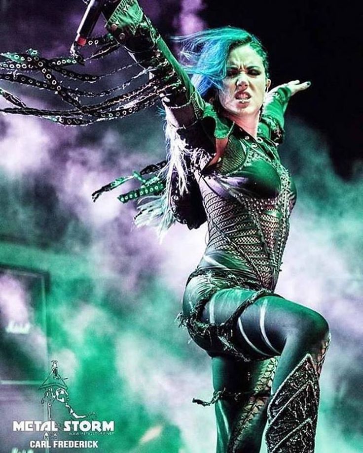 a woman dressed in green and black performing on stage with her arms spread out to the side