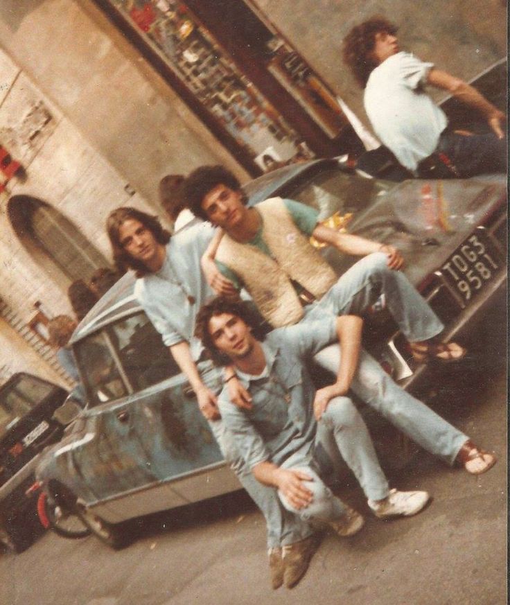 four young men posing in front of an old car