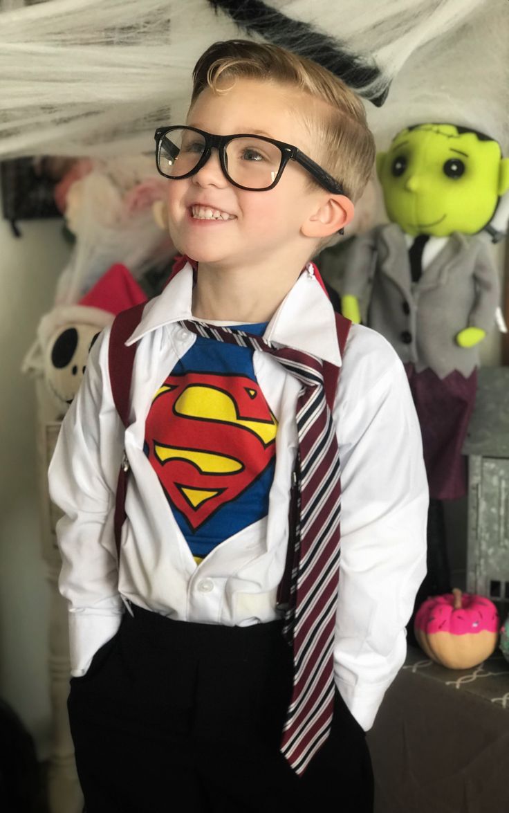 a young boy wearing a superman shirt, tie and eyeglasses standing in front of stuffed animals