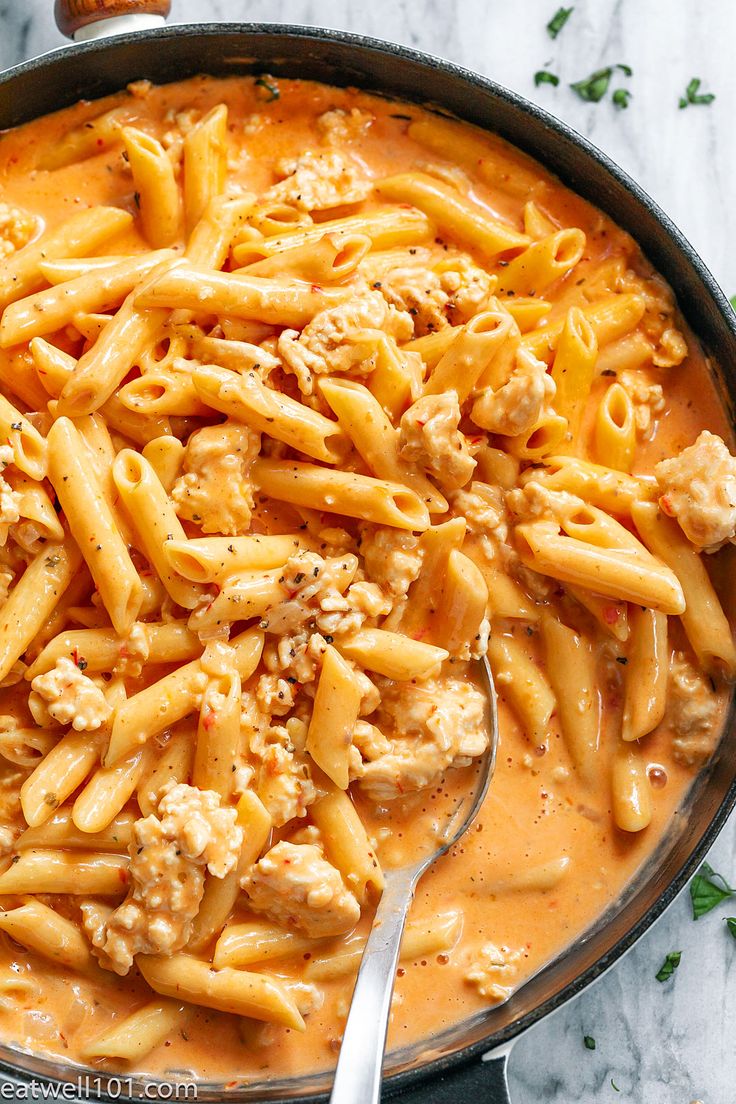 a skillet filled with pasta and meat in sauce on top of a marble counter