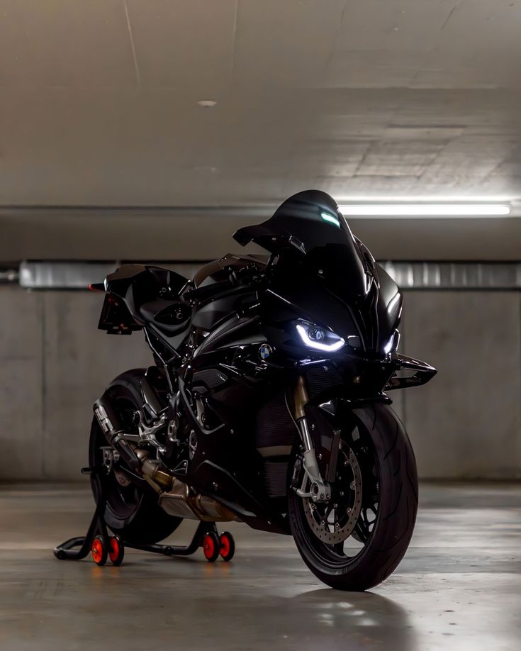 a black motorcycle parked in an empty parking garage with its lights on and red wheels