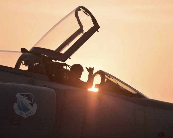 a fighter jet with the sun setting in the background and its cockpit door partially open