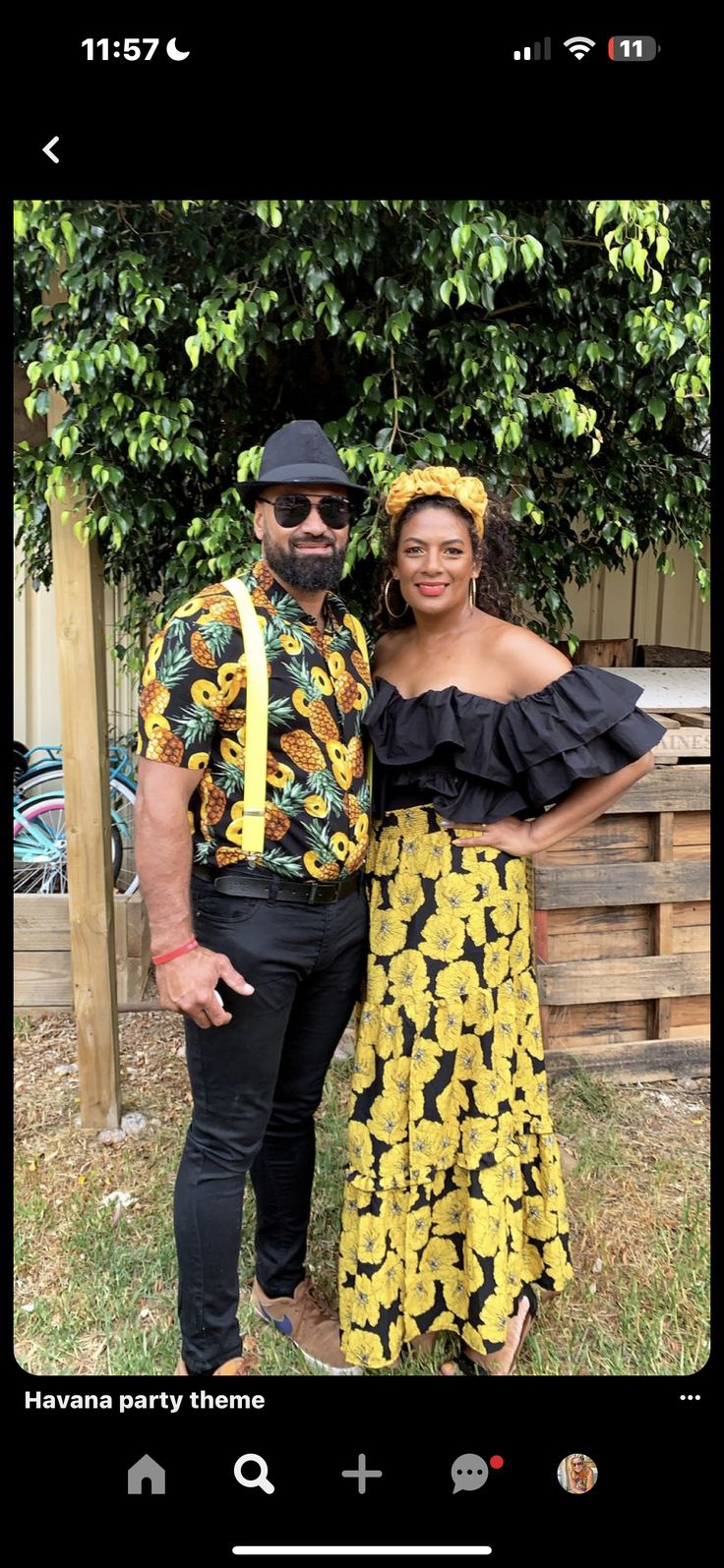 a man and woman standing next to each other in front of a tree with yellow flowers on it