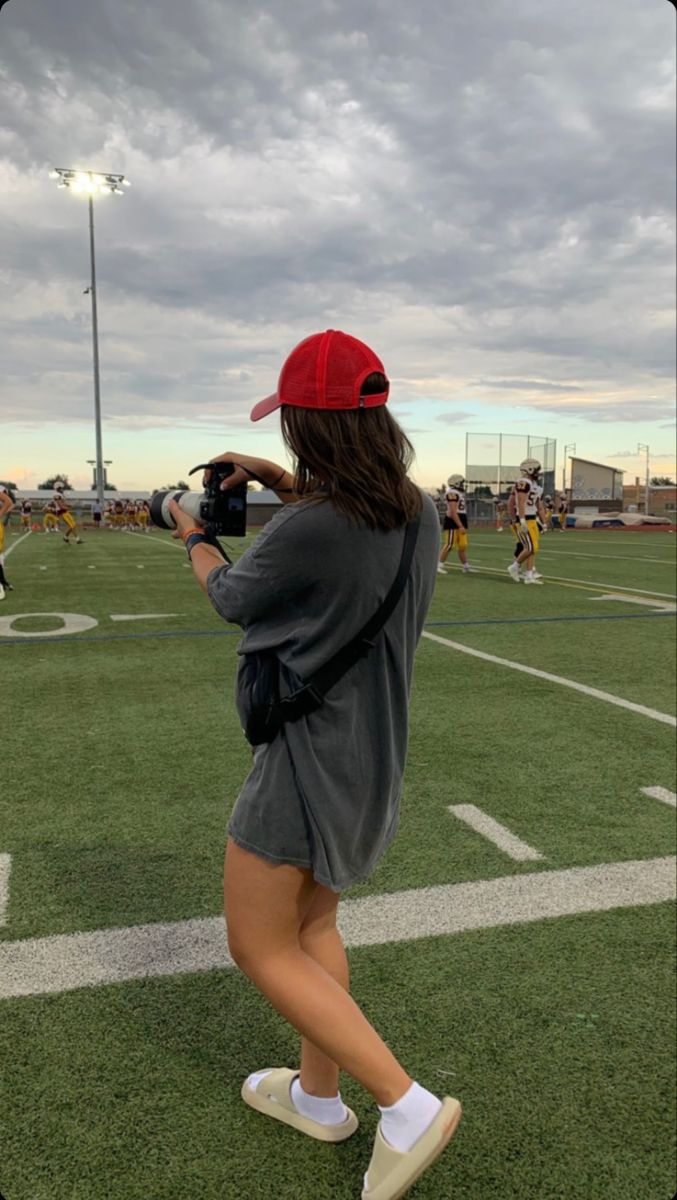 a woman in grey shirt and red hat on field