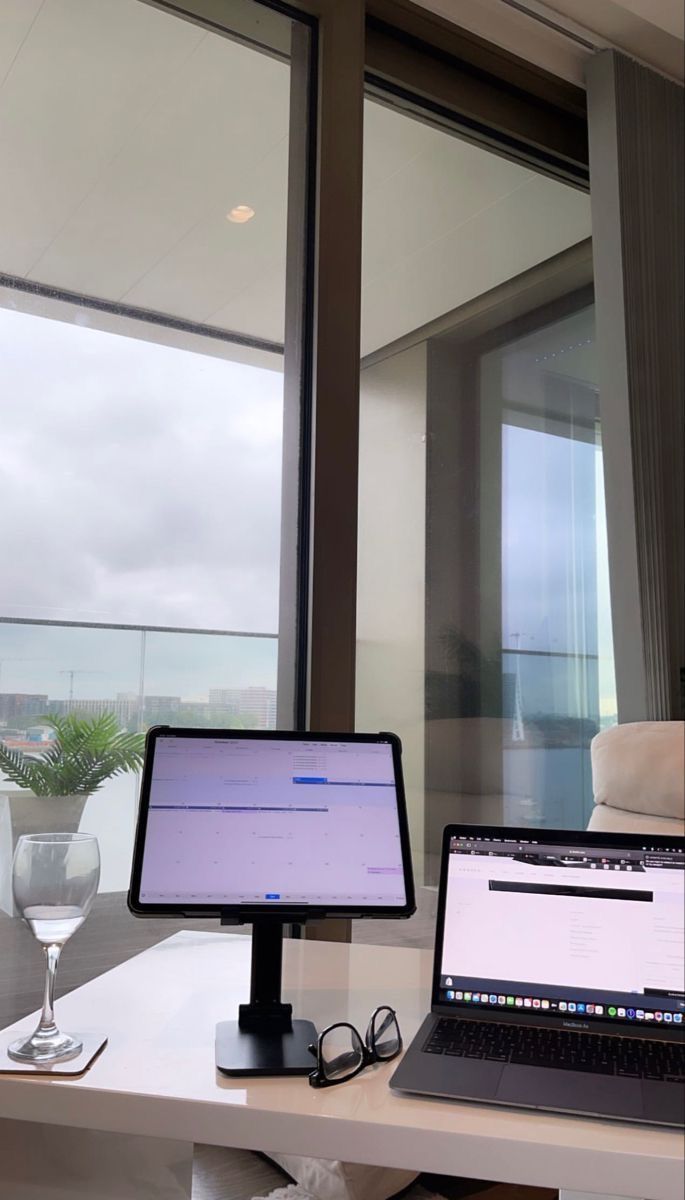 two laptops and a monitor on a desk in front of a window overlooking the ocean