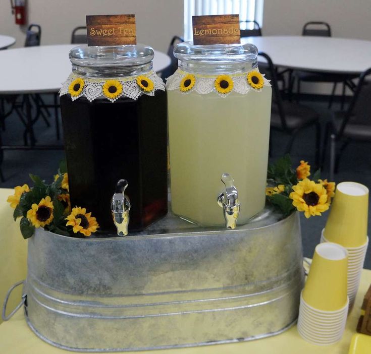 two jars filled with liquid sitting on top of a metal barrel covered in sunflowers