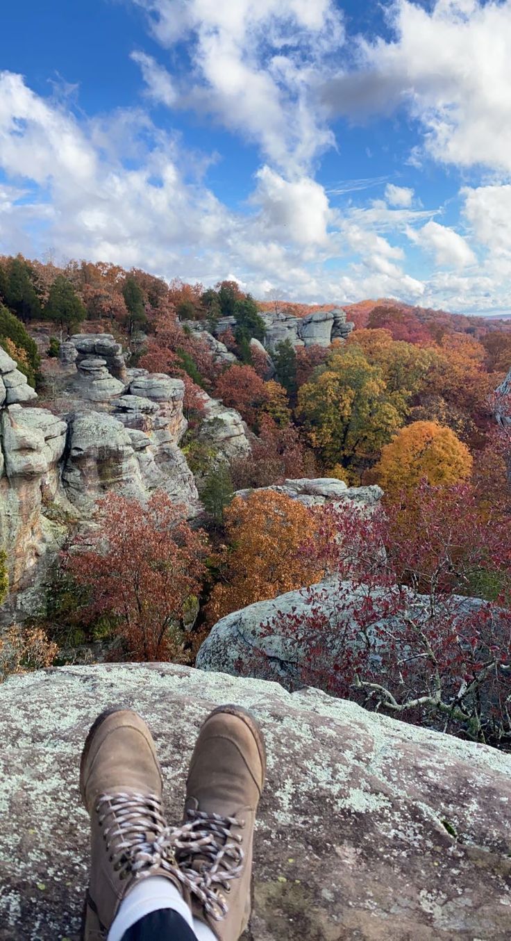 a person's feet on top of a large rock with trees in the background