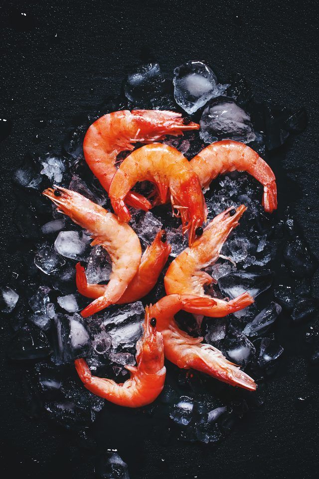 raw shrimp on ice with lemons and black pepper in the background, top view