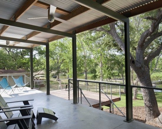 an outdoor covered patio with chairs and trees in the background, overlooking a grassy area