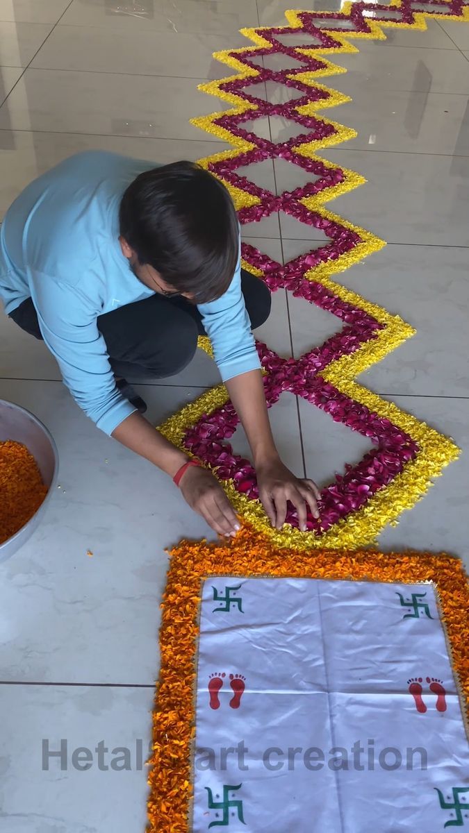 a person kneeling down on the ground with flowers in front of them and making a design