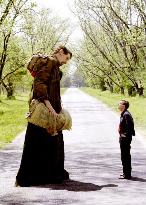 a man standing on the side of a road next to a woman in a long dress