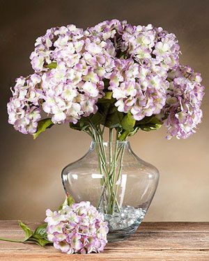 a vase filled with purple flowers sitting on top of a wooden table next to another vase