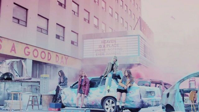 a group of women standing on top of a car in front of a movie theater