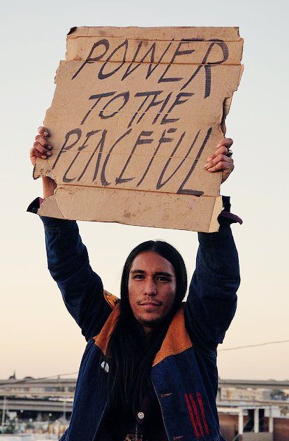 a man holding up a sign that says power to the peaceful on it's face