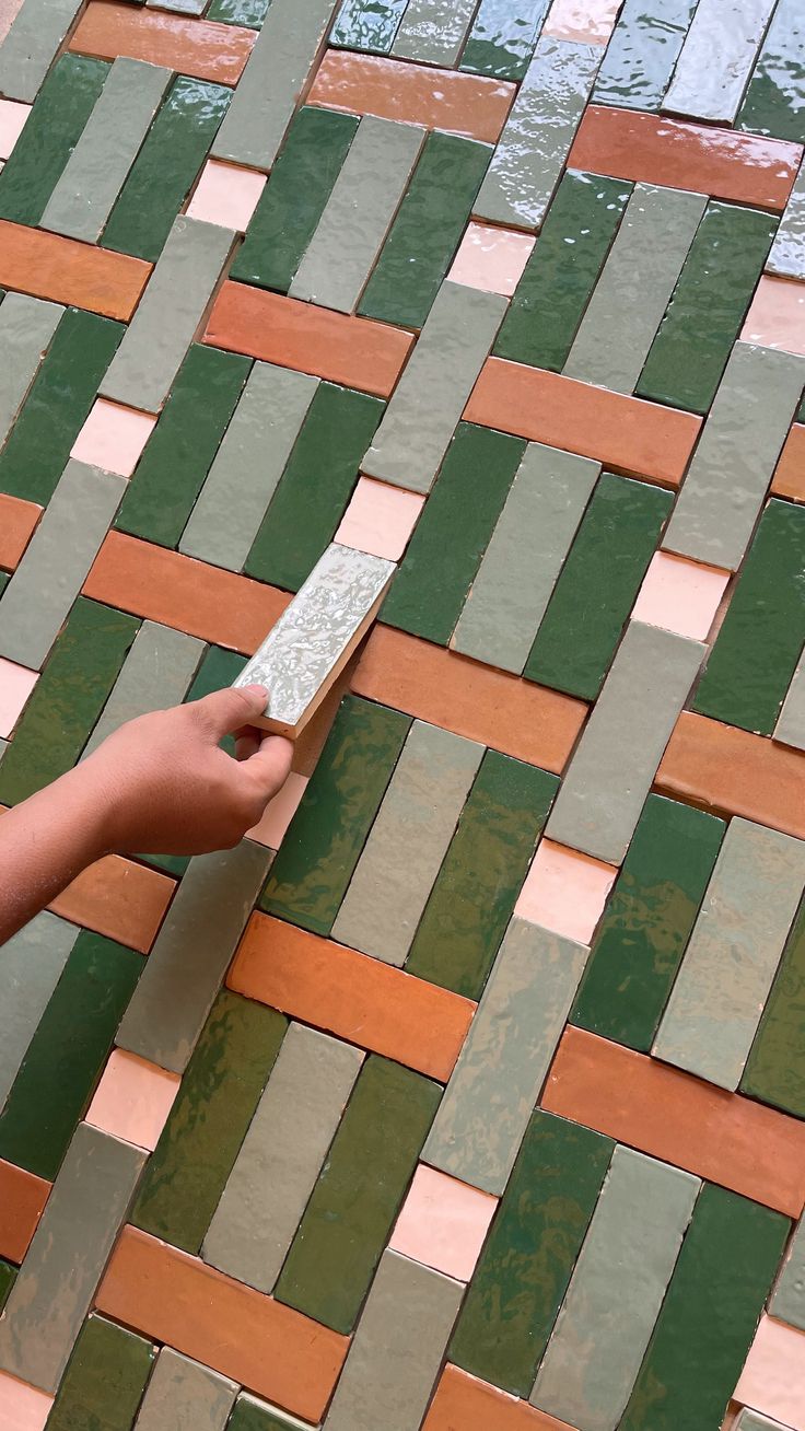 a person holding a remote control in their hand on a tiled floor that is green and brown