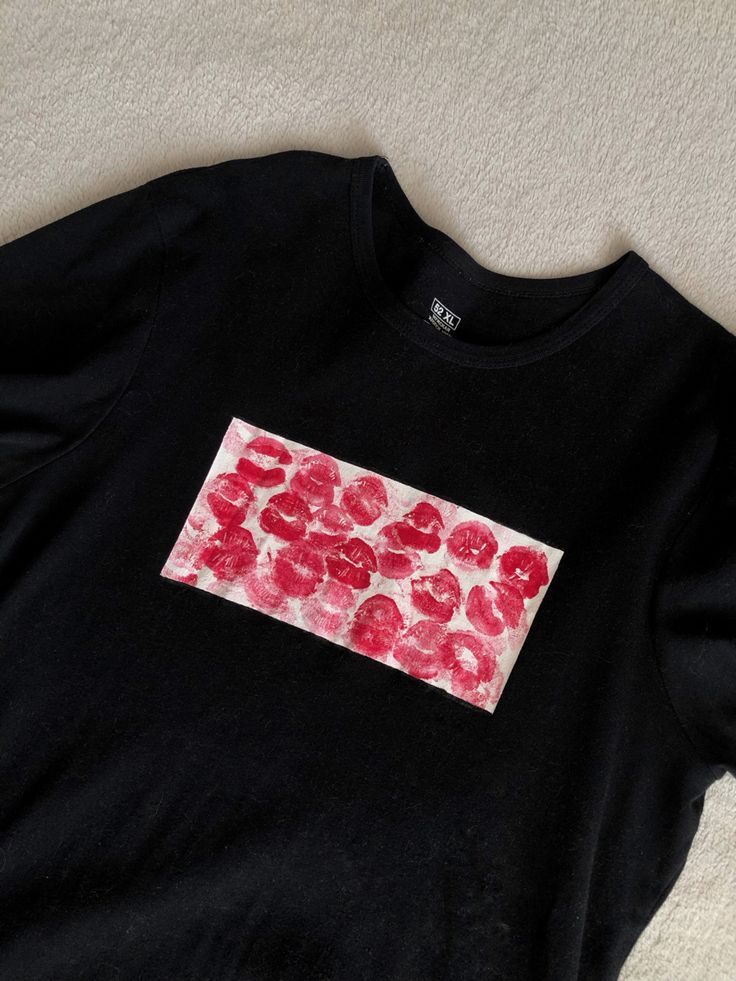 a black t - shirt with red and pink flowers on the front, sitting on a white carpet