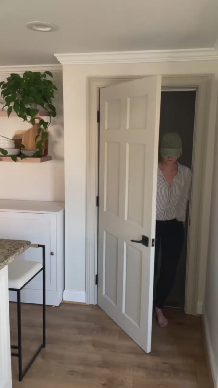 a man standing in front of a white door next to a kitchen counter and table