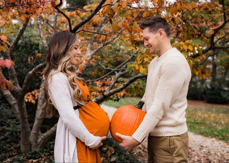 a pregnant couple holding pumpkins in their hands