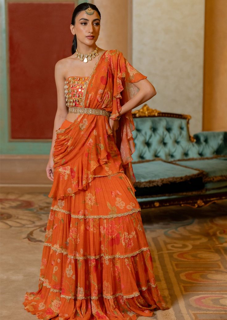 Featuring the rust pre-draped chiffon sari in our signature print , paired with kowri shell and coin detailed corset blouse. It is styled with our signature cutdana belt. Floral Ruffle Saree, Orange Saree Look, Paulmi And Harsh, Mehendi Dresses, Ruffled Saree, Scallop Embroidery, Suit Neck Designs, Punjabi Suit Design, Maharani Designer Boutique