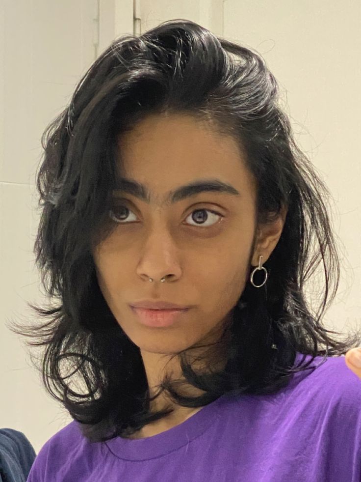 a woman with long black hair and blue eyes wearing a purple shirt looking at the camera