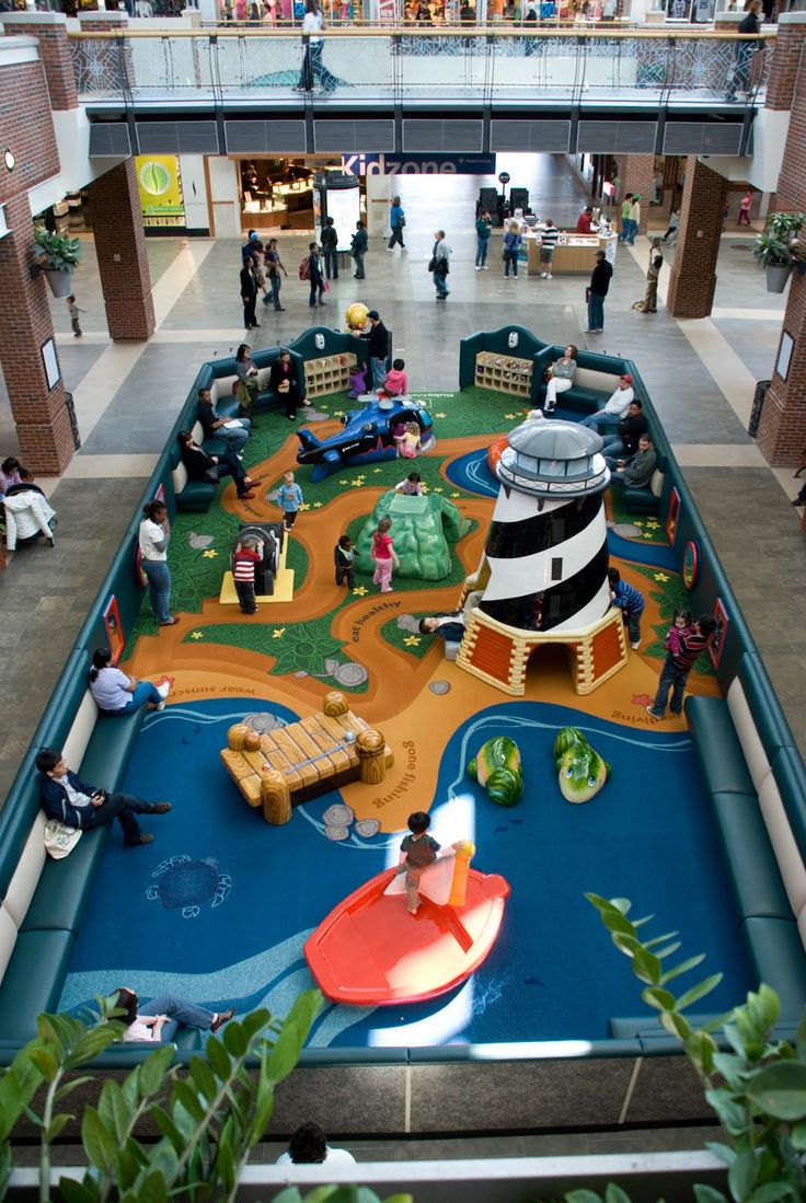 an indoor play area in a mall with children playing on the ground and people walking around