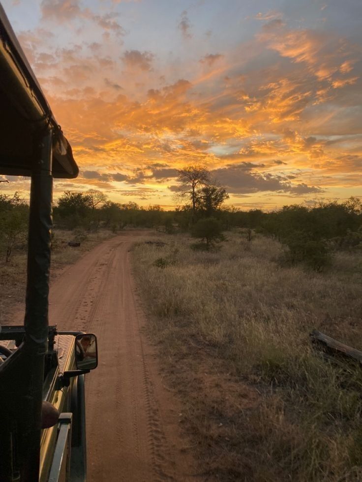 the sun is setting in the distance as people ride on a safari vehicle down a dirt road