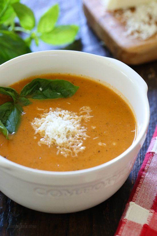 a bowl of tomato soup with parmesan cheese and basil on the side, next to bread