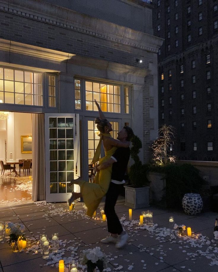 two people dancing in front of a building with candles on the ground and flowers all around them