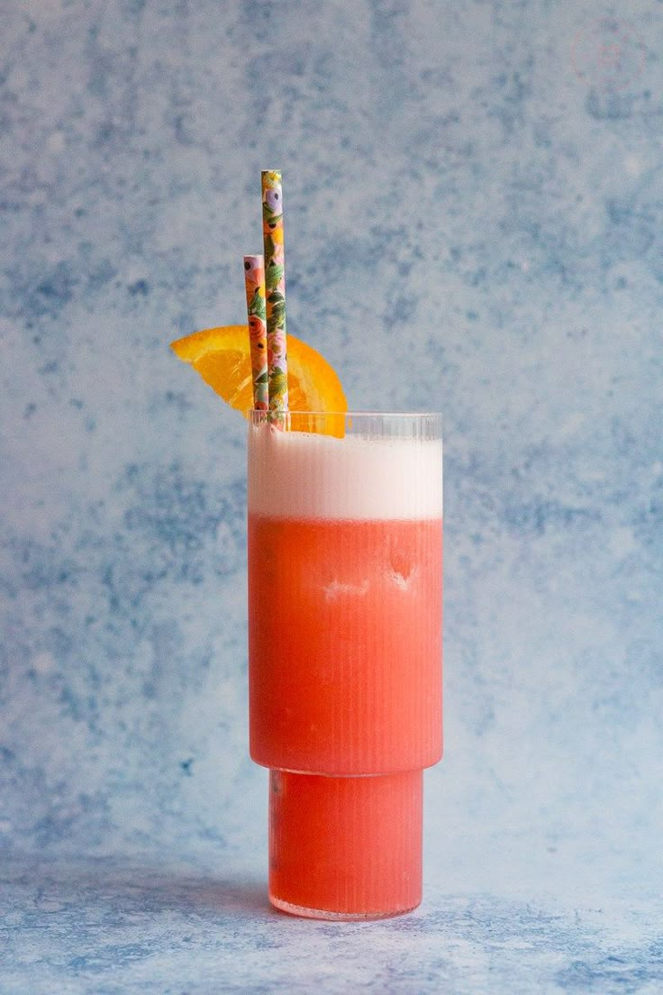 a tall glass filled with orange juice and two straws sticking out of the top