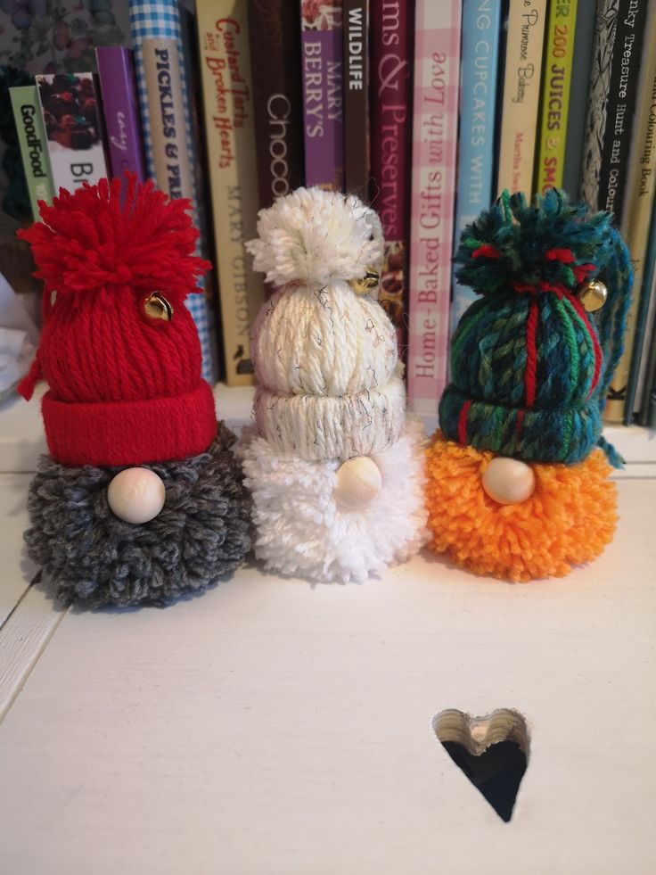 three knitted hats sitting on top of a table next to a book shelf filled with books