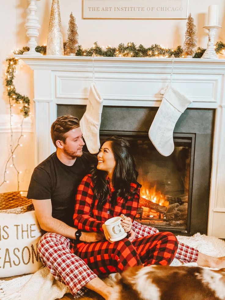 a man and woman sitting in front of a fireplace with christmas stockings on their heads