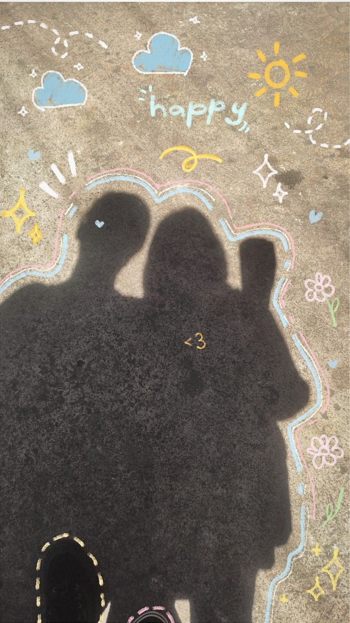 the shadow of two people standing in front of a chalk drawing on the ground that says happy