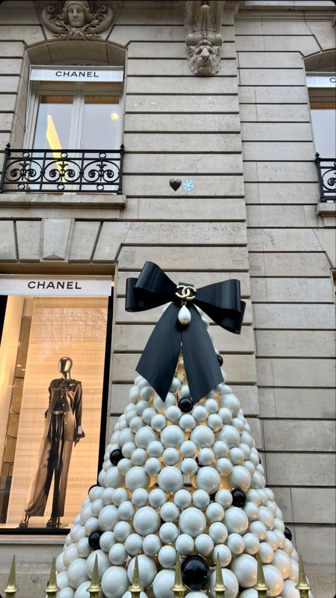 a christmas tree made out of balls in front of a building with a black bow