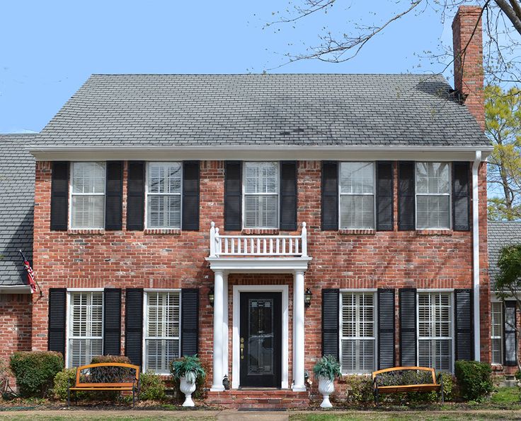 a large brick house with black shutters and white trim on the front door is shown