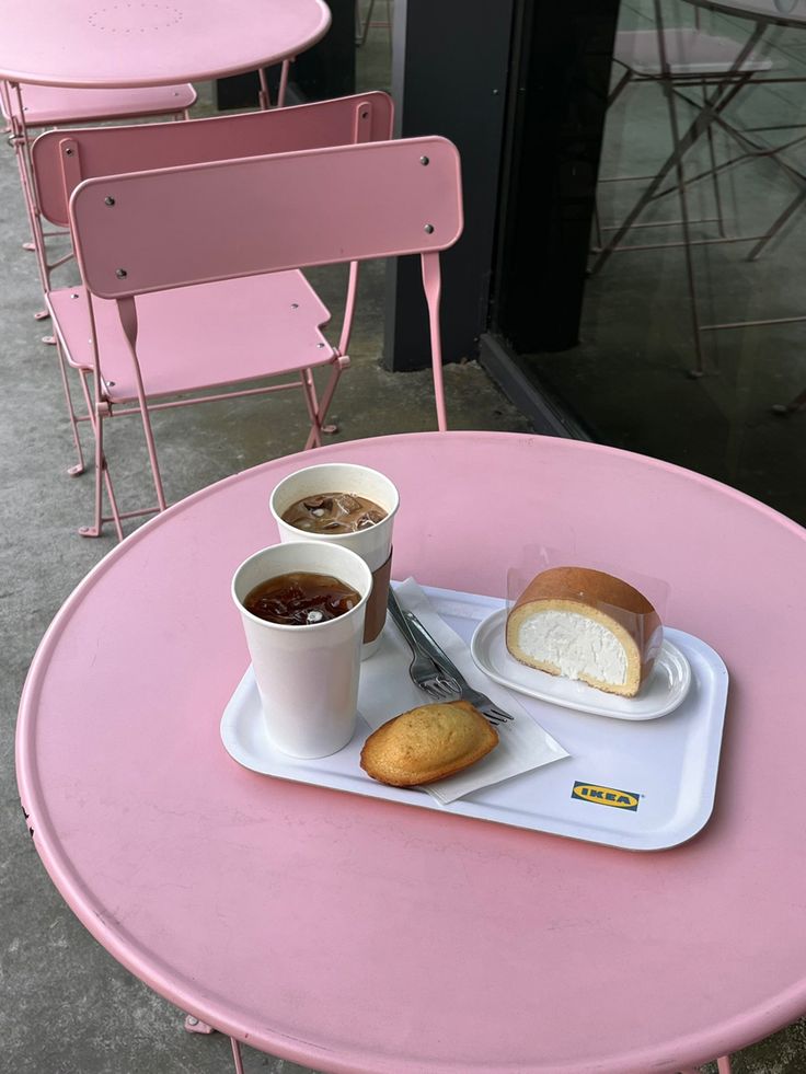 a pink table topped with two plates of food and cups of coffee next to each other