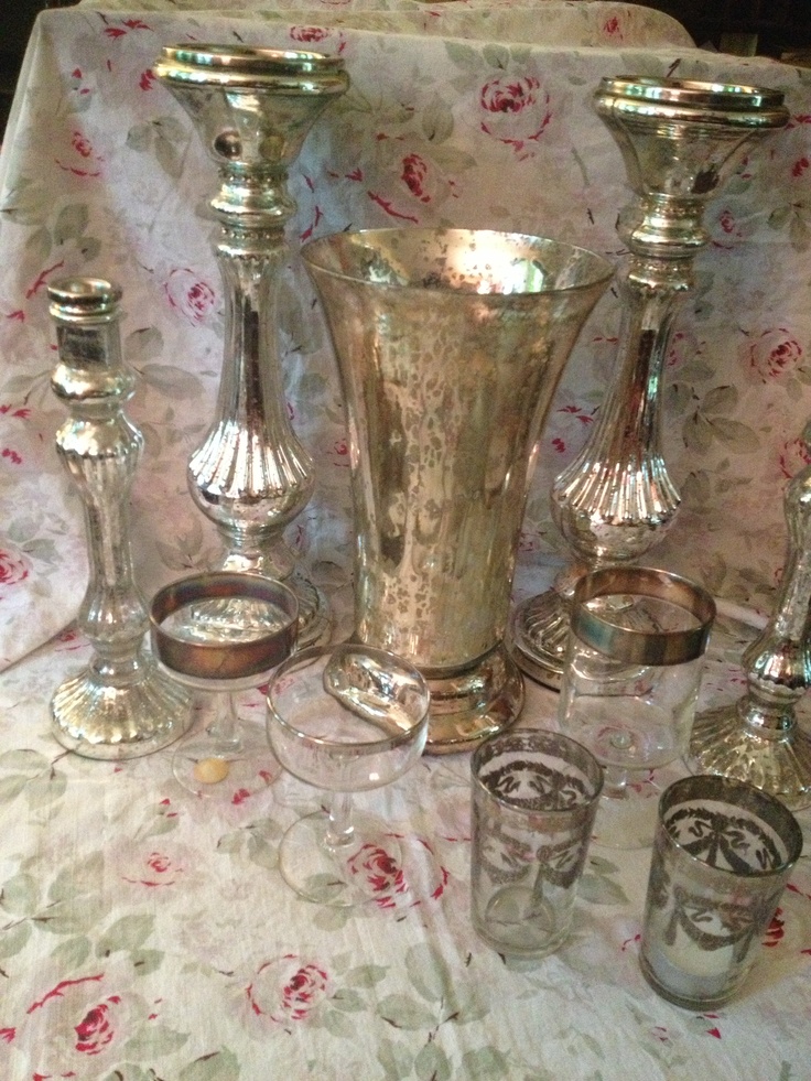 a table topped with lots of silver vases and glasses on top of a table cloth