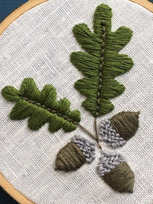 a close up of a embroidery on a piece of cloth with leaves and acorns