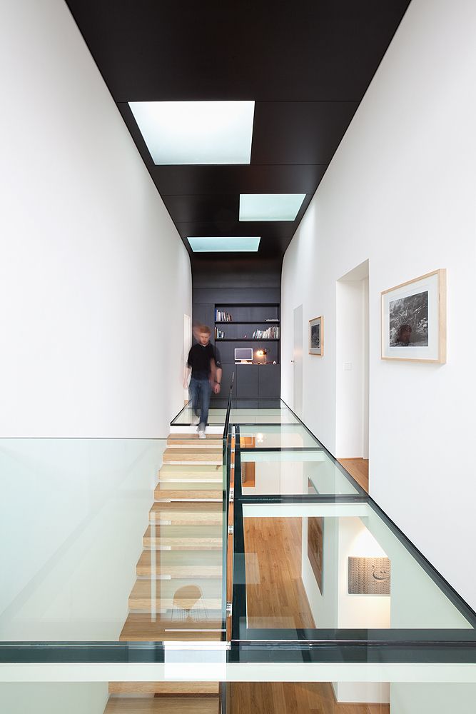 a man walking down a set of stairs in a house with glass railings on both sides