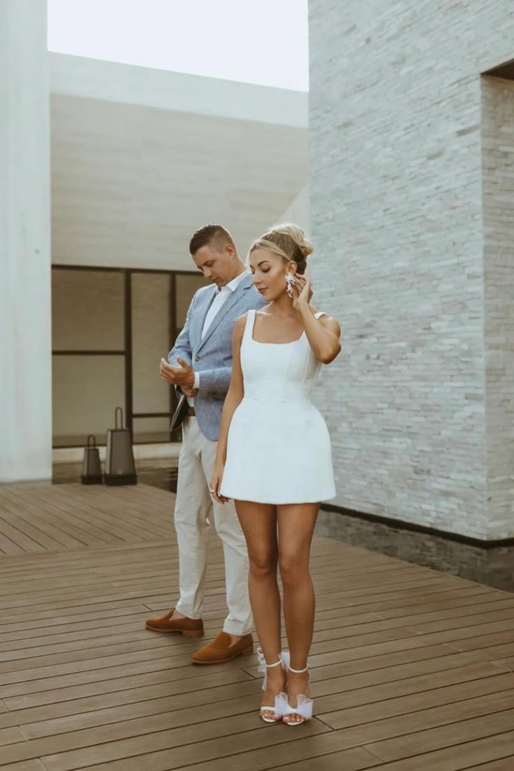 a man standing next to a woman in a white dress on a wooden floor while talking on a cell phone