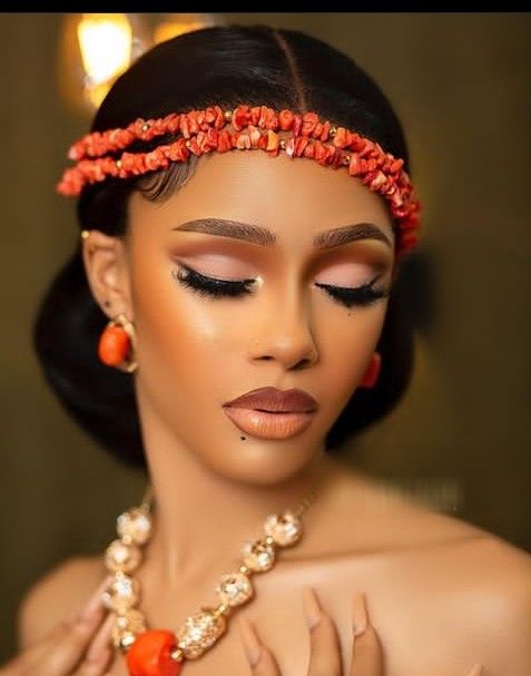 a woman wearing an orange and red headpiece with pearls on her hair, holding onto a beaded necklace