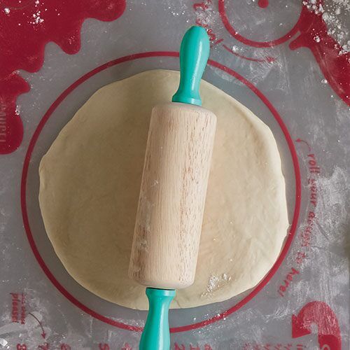 a rolling dough on top of a red and white plate with a blue roller in the middle