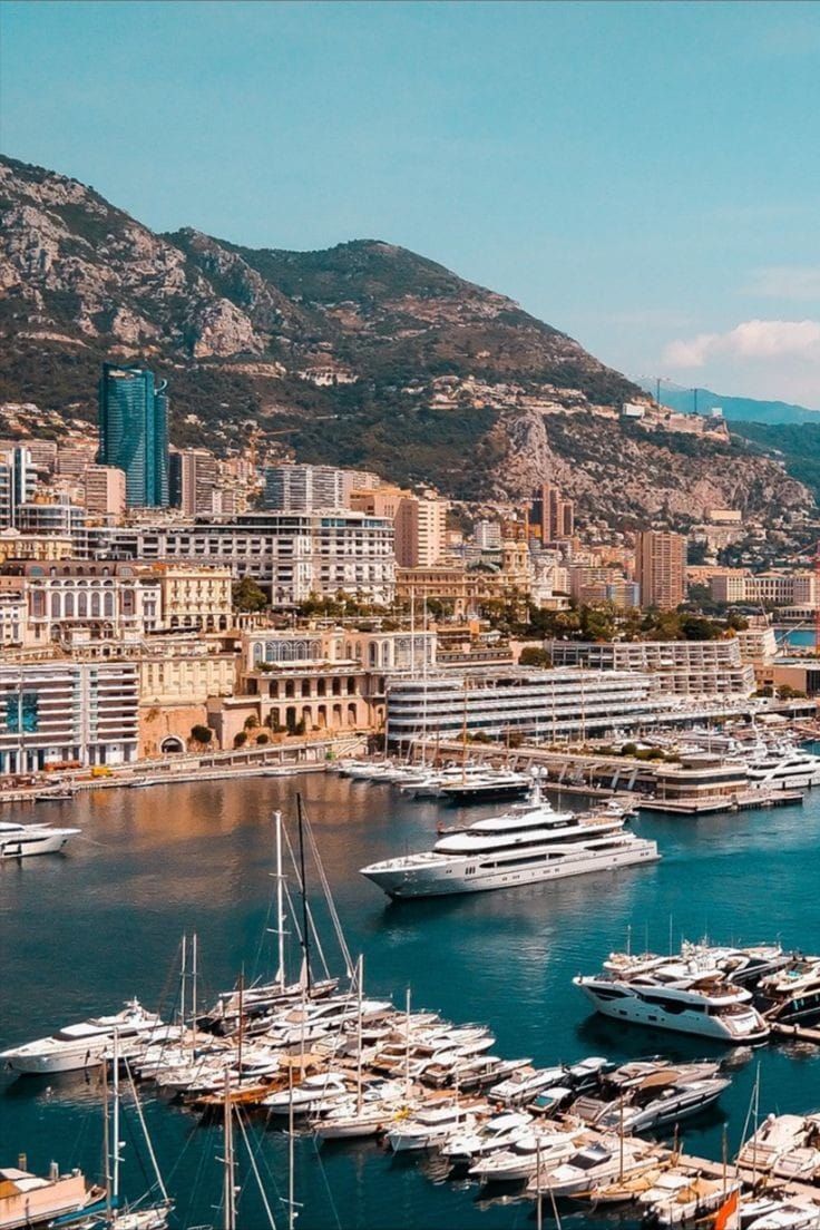 boats are docked in the water near some buildings and mountains, with a city in the background