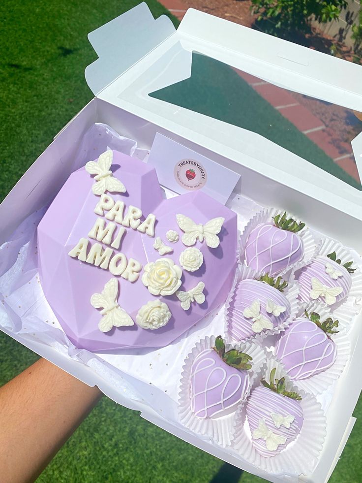 a box filled with purple and white chocolate covered in frosting next to a person's hand