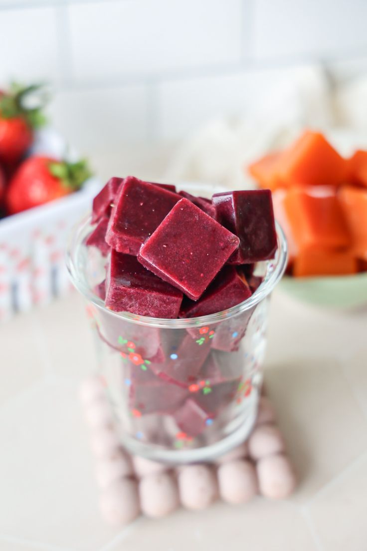 a glass filled with candy sitting on top of a counter next to fruit and veggies