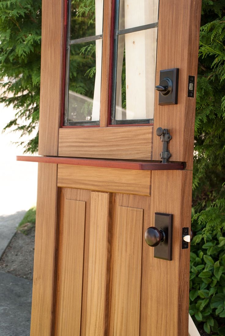 a wooden door with two windows on the side of it and some bushes behind it